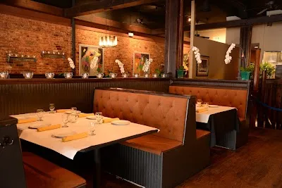 Elegant Thai restaurant interior with booth seating, white tablecloths, and brick walls.